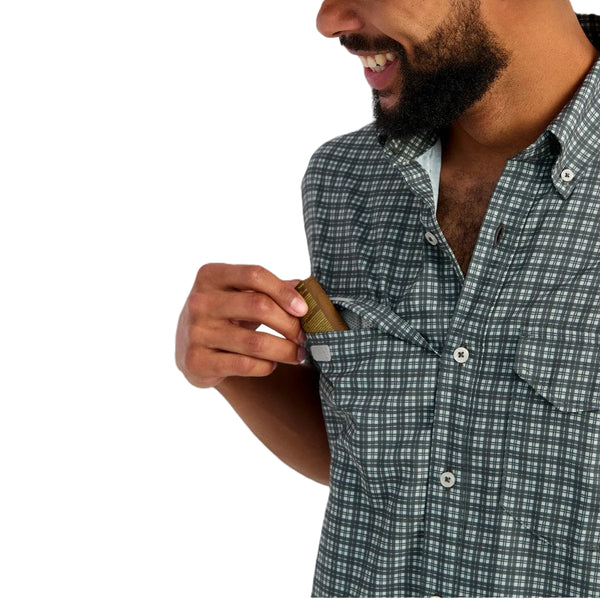 Man wearing a mini checkered print Huk Short-Sleeve Tide Point Shirt showing pocket details on a white background.