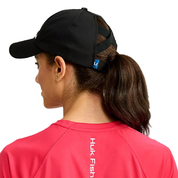 Person wearing the Huk Women's Pony Tail Hat showing the back designed to accommodate ponytails on a white background.
