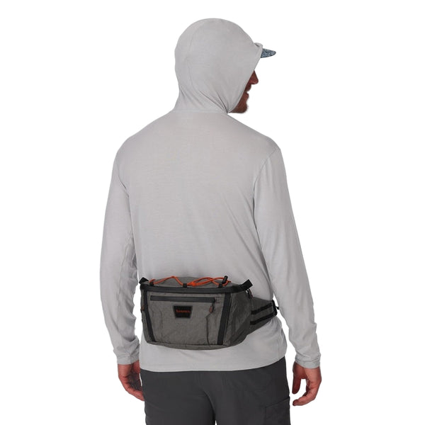 Person wearing a light gray hoodie with a Simms Scout Hip Pack on a white background.