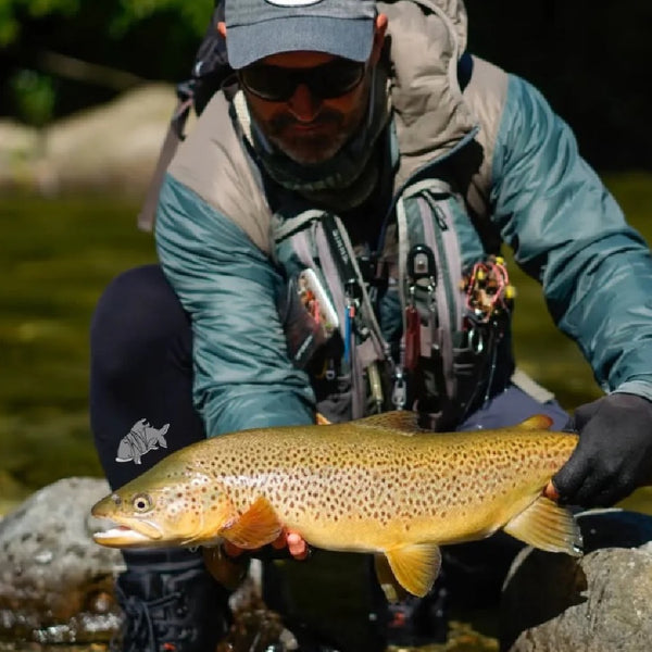 Person wearing Backcountry Skinz Airblitz Neoprene Pants holding a large brown trout by a river.