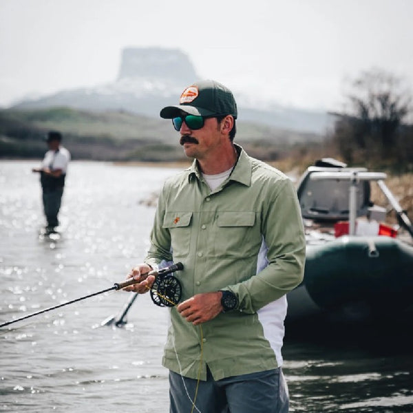 Man wearing the Backcountry Skinz Aerodrift Shirt fly fishing on a river with mountains in the background
