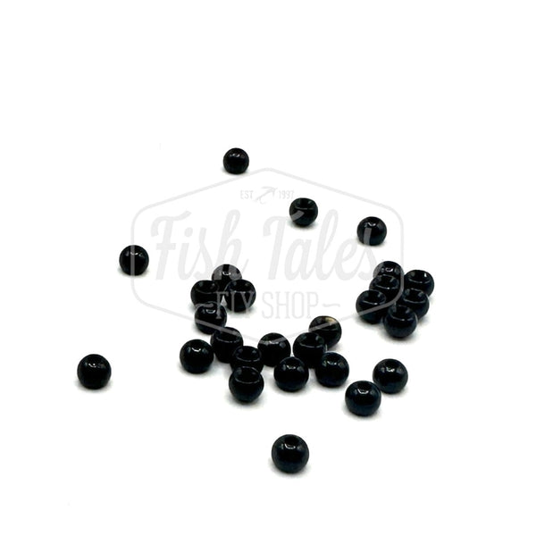 A collection of black brass fly tying beads scattered on a white surface.
