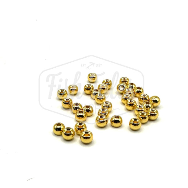 A collection of gold brass fly tying beads scattered on a white surface.