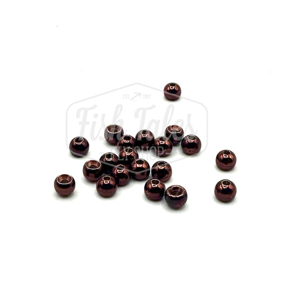 A collection of metallic coffee color brass fly tying beads scattered on a white surface.