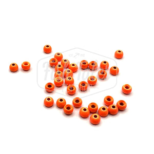 A collection of orange brass fly tying beads scattered on a white surface.