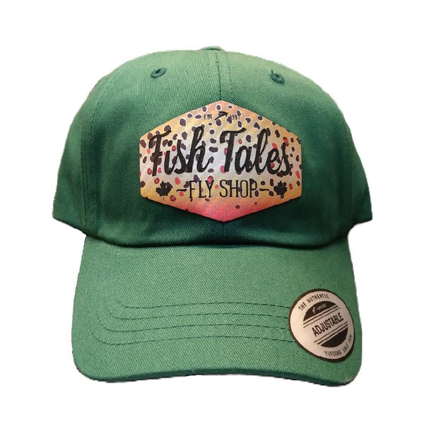 Green ball cap with brown trout 'Fish Tales Fly Shop' logo patch, on a white background.