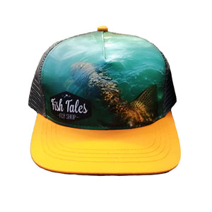 Trucker hat with charcoal mesh back, gold brim, and fish design with 'Fish Tales Fly Shop' logo on the front panel, shown on a white background.