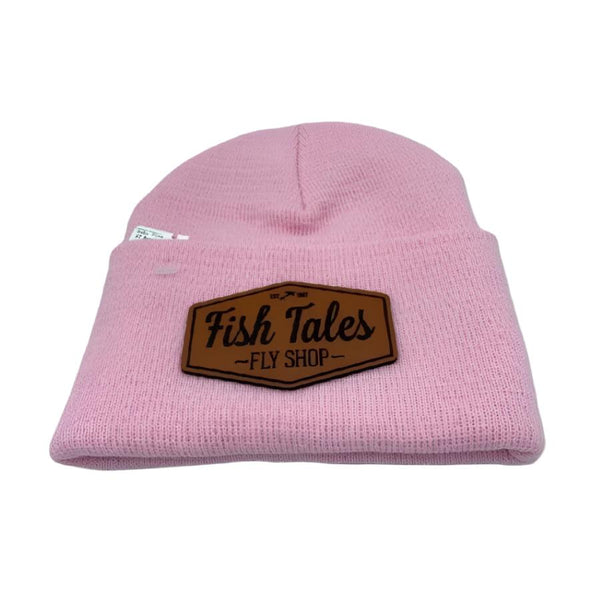 Front of a baby pink knit beanie hat with a fish tales fly shop logo leather patch on a white background. 