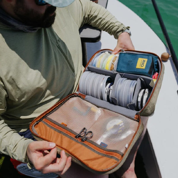 Person holding a sand and tan Fishpond Honco Reel Case on a boat with fishing gear inside.