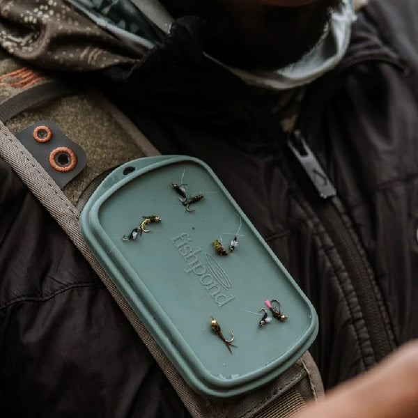Person wearing a Fishpond sling pack bag with a Fishpond Tacky Grande Mag Pad in Smoke Grey attached to strap loaded with flies.