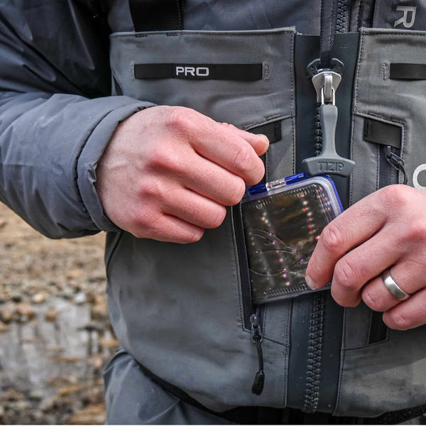 Person placing a blue Fulling Mill pocket fly box loaded with fishing flies into a front wader pocket.