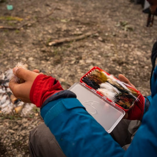 Person outdoors holding a red Fulling Mill streamer box full of streamers with one held in the other hand.