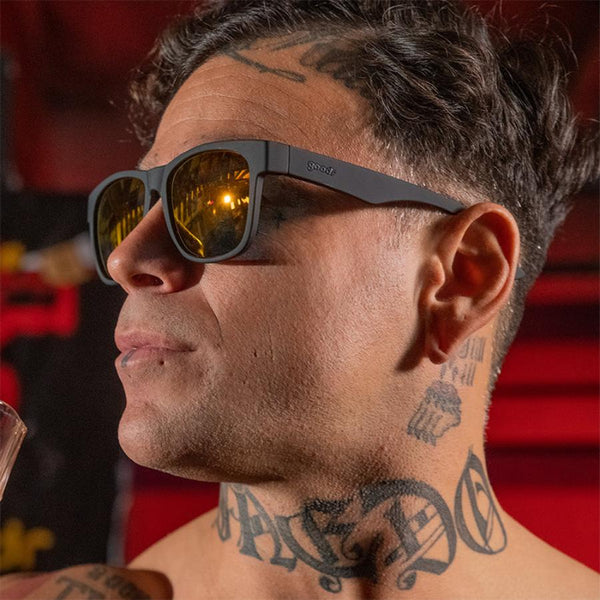 a man with tattoos wearing Goodr BFG Beelzebub's Bourbon Burpees Polarized Sunglasses on a red background