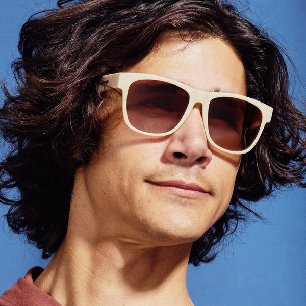 Person wearing beige Goodr BFG Big Pajama Llama Drama sunglasses with a gradient lens on a blue sky background.