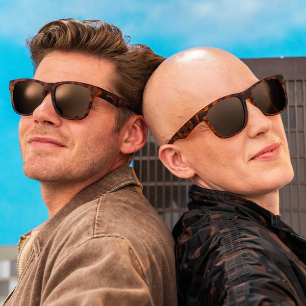 Two people wearing a pair of tortoiseshell print Goodr BFG polarized sunglasses with a wide-fitting design on an urban background.
