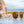 Wood patterned Goodr Circle G Bodhi's Ultimate Ride sunglasses with brown lenses in a beach setting with an ocean background.