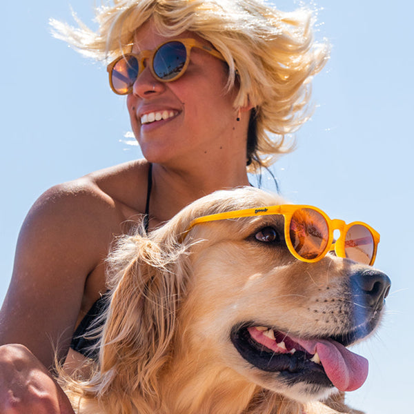 Woman and dog wearing wood patterned Goodr Circle G Bodhi's Ultimate Ride sunglasses against a clear blue sky.
