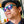 Person wearing teal framed Goodr Circle G I Pickled These Myself Sunglasses with lilac lenses with a blurred kitchen background.