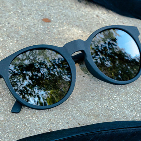Black Circle G sunglasses with reflective lenses on a concrete surface.