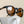 Coffee cup with Goodr Circle G Nine Dollar Pour Over Sunglasses with tortoiseshell frame over an off-white background.