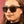 Close-up of a person wearing Goodr Grand G tortoiseshell sunglasses with a pink background