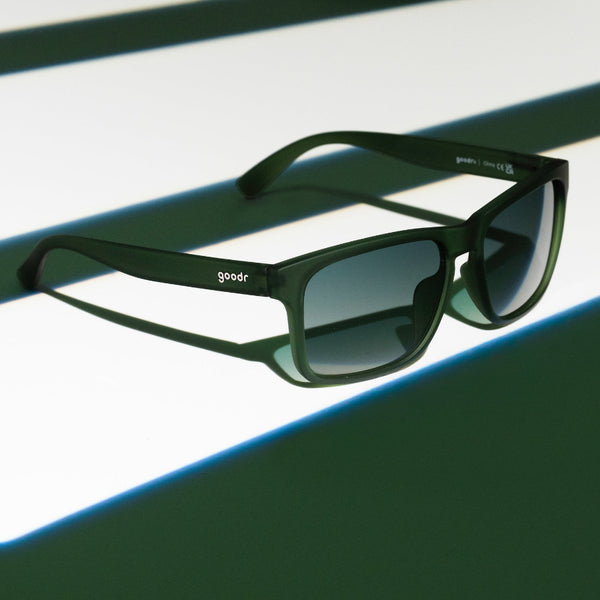 Green sunglasses with 'goodr' branding on a green and white striped surface.
