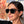 Person wearing a pair of matte black Goodr LFG sunglasses with a level on her head with a blurred background.