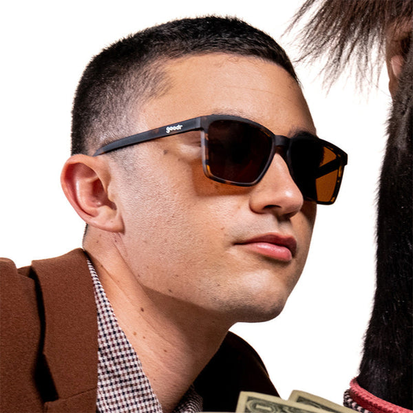 Person wearing Goodr LFG Sunglasses with tortoiseshell frame and brown lenses on a white background.