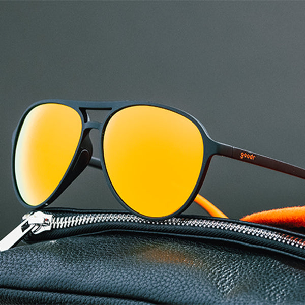 Goodr MACH G Call Me Tarmac Daddy sunglasses sitting on a leather jacket against a gray background.