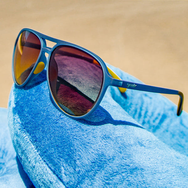 Goodr Mach G Frequent Skymall Shoppers Sunglasses with blue frame and yellow accents on a blue and tan background.