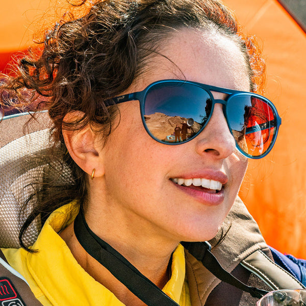 Woman wearing Goodr Mach G Frequent Skymall Shoppers Sunglasses with a reflective orange background.