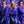 3 people with octopus arms wearing purple suits and  Goodr Mach G aviator sunglasses with blue-tinted lenses on a sparkly background.