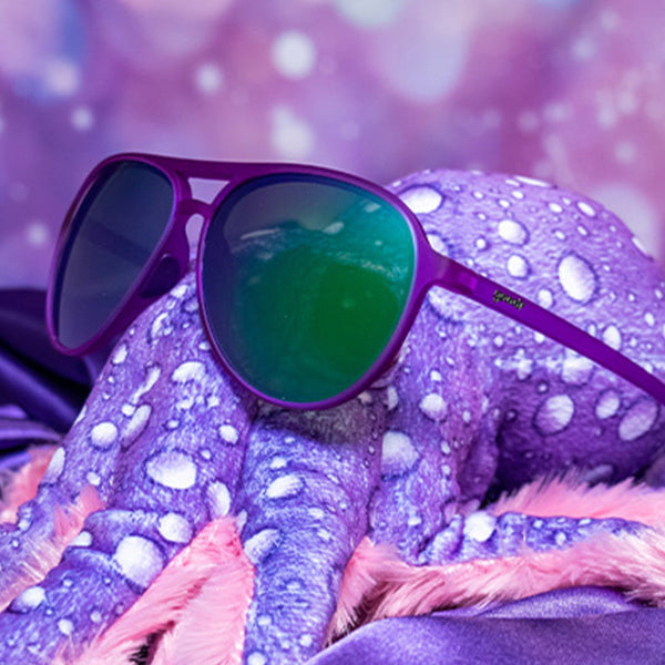 Purple Goodr Mach G aviator sunglasses with blue-tinted lenses on  an octopus stuffie over a light purple background.