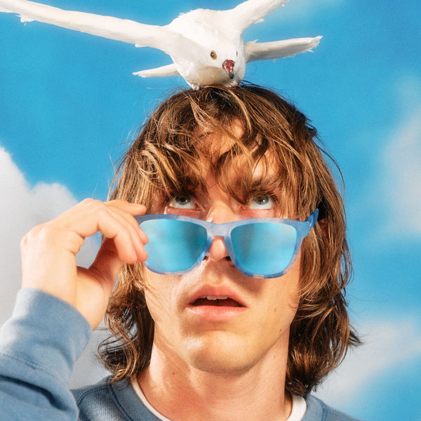 Person wearing blue Goodr OG Binge Watching the Sky sunglasses with a white dove on their head against a blue sky background.
