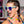 Woman with French braided hair wearing the Goodr OG Electric Dinotopia Sunglasses on a colorful background.