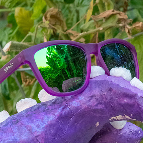 Purple Goodr OG Gardening With a Kraken sunglasses with blue lenses on a squid tentacle in a garden.