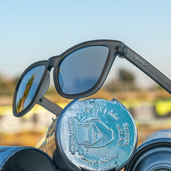 Gray Goodr OG Going To Valhalla Witness sunglasses with mirror lenses on metal tube caps on a blurred background.