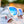 White Goodr OG Iced By Yetis sunglasses with blue lenses on a some bottles on ice over a blurred background.