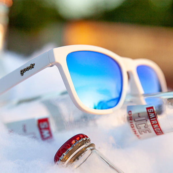 White Goodr OG Iced By Yetis sunglasses with blue lenses on a some bottles on ice over a blurred background.