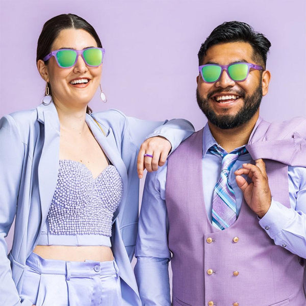 Two people wearing pair of lilac purple Goodr OG sunglasses with purple suits on a purple background.
