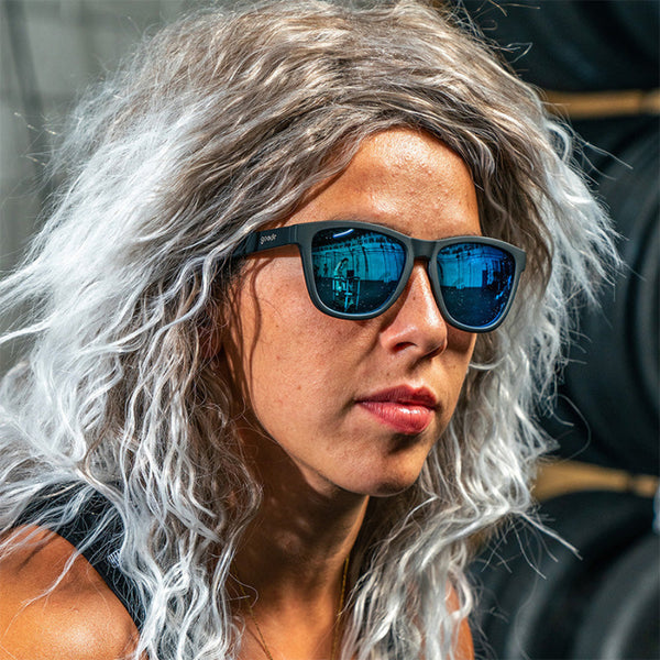Person with gray hair wearing reflective Goodr OG sunglasses in an urban setting.