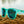 Turquoise Goodr OG sunglasses with green lenses on a textured surface and neutral background.
