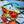 Goodr OG Sunglasses with blue and yellow frame and pink lenses on a glass surface..
