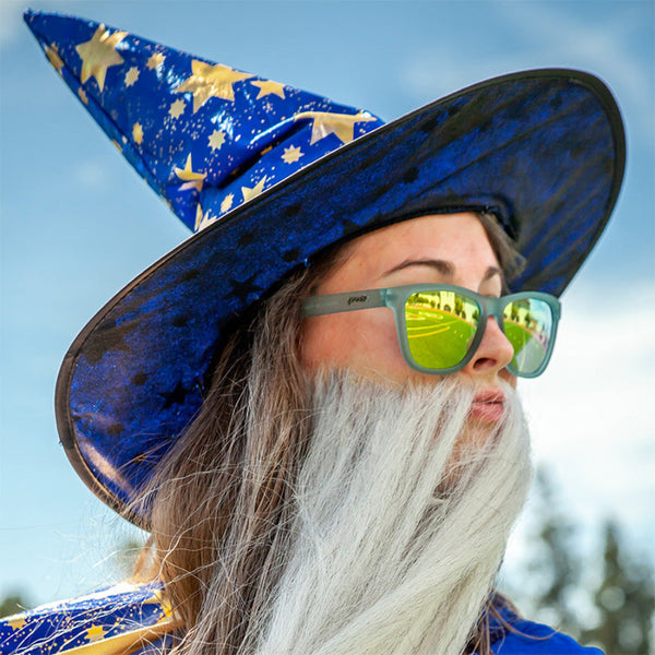 Person wearing a blue wizard hat with star patterns and Goodr OG Sunbathing With Wizards Sunglasses against a blurred natural background.