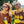 Two people wearing Goodr OG Three Parts Tee Sunglasses with a brown frame and black lenses on a blurred outdoor background.