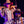 Two people dressed as prospectors  wearing Goodr PHG Sunglasses with pink lenses and dark grey frames in front of a purple curtain.