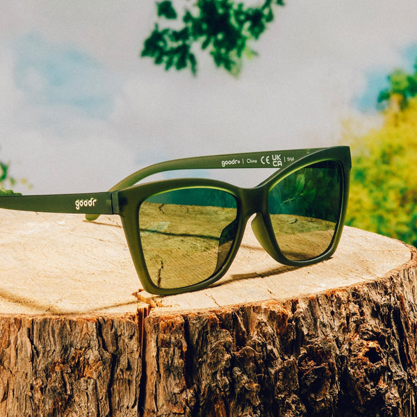 Green Goodr POP G Garnish Me in Greens Sunglasses sitting on a tree stump with blue sky and green foliage in the background.