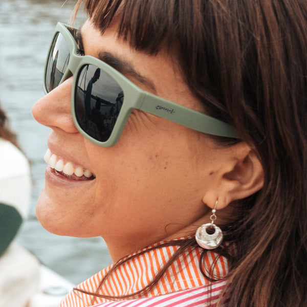 Woman wearing Goodr Tidal G green sunglasses with a blurred background.