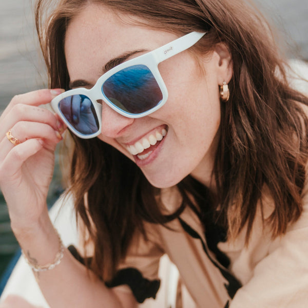 Woman wearing light blue Goodr Tidal G sunglasses with blue lenses, smiling outdoors.