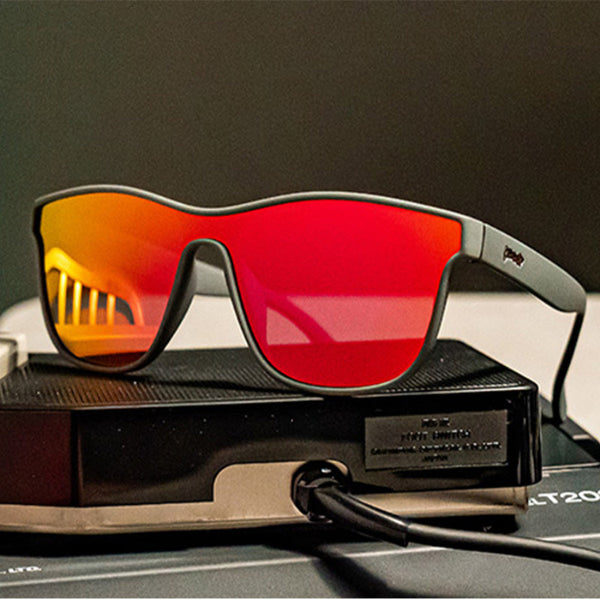 Goodr VRG Voight Kampff Vision Sunglasses with mirrored orange lenses and black frame sitting on electronics over a grey background.